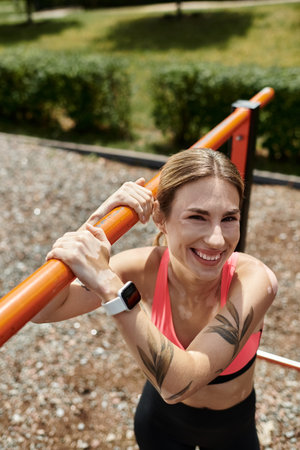A young woman with vitiligo, wearing a pink crop top, smiles as she works out on a horizontal bar in...