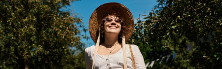 A young woman wearing a straw hat and sunglasses smiles brightly as she walks through a summer...