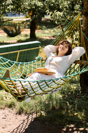 A young woman in a white dress relaxes in a hammock, enjoying the summer sun in a lush garden.の写真素材