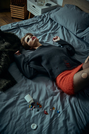A stylish woman lies on a bed, surrounded by scattered pills and an overturned bottle.