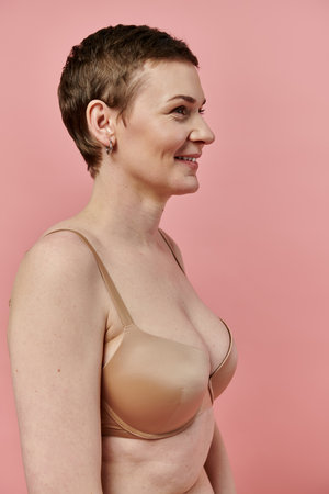 A woman with short hair, wearing a bra, smiles while looking off to the side against a pink background.の写真素材