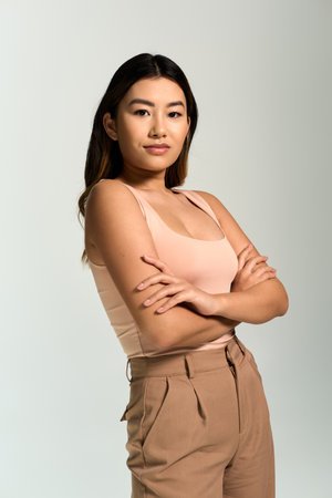 Confident woman with dark hair, arms crossed, in light pink tank top and brown pants.の写真素材