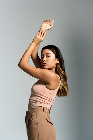 A woman in a pink tank top and tan pants poses against a grey background.の写真素材