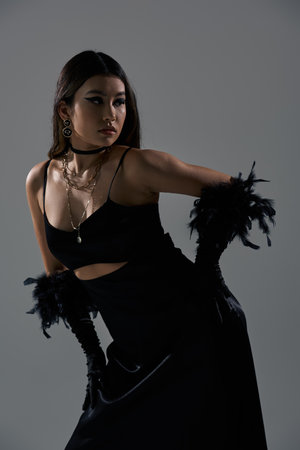 A woman in black, adorned with feathers, poses against a gray backdrop.の写真素材
