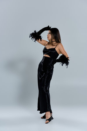 A woman in a black dress and feather gloves poses in a studio.