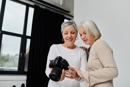 A mature lesbian couple reviews photos together in a photography studio, one woman holds the camera while the other looks at the screen.の写真素材