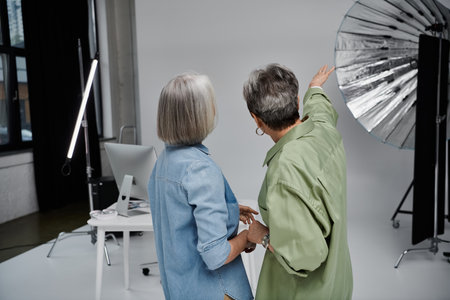 A lesbian couple in a photo studio, one working as the photographer and the other as the model, discuss lighting choices.の写真素材