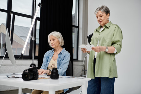 A mature lesbian couple works on a photo shoot in a studio, one reviewing images while the other is a model.の写真素材