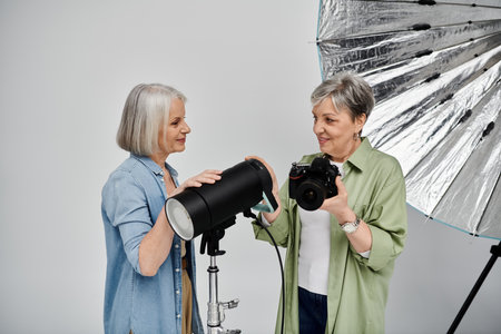 Two mature lesbian women are in a photo studio. One is holding a camera, the other adjusting a studio light.の写真素材
