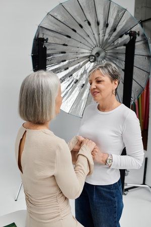 A lesbian couple in a studio, one taking photos, the other modeling. They hold hands and share a loving glanceの写真素材