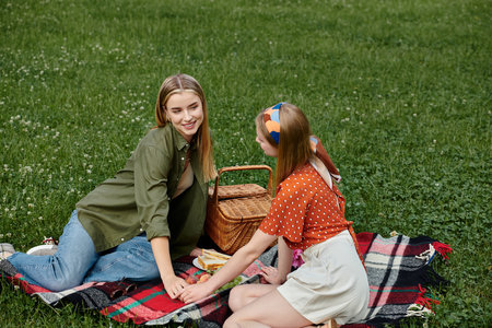 Two young women share a warm moment during a picnic in a green park.の写真素材