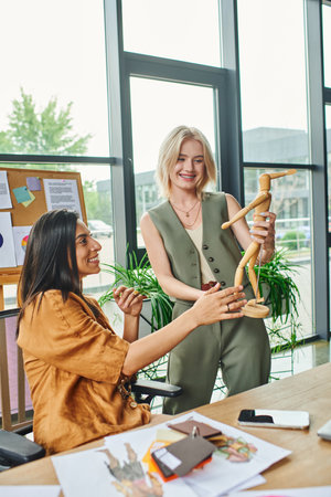 Two women discuss designs using a wooden mannequin in a modern office setting.の写真素材