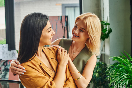 lesbian couple, dressed in smart casual attire, stand in a cozy workspace and look at each other with smiles.の写真素材