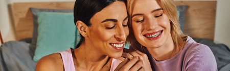 Two women, one with dark hair and the other with blonde, smile warmly as they hug each other in their cozy home.の写真素材