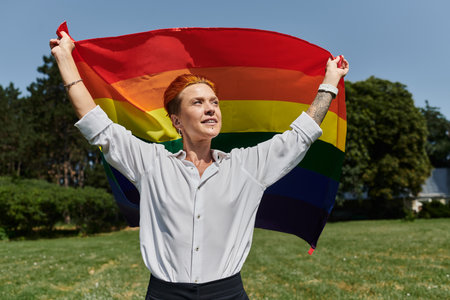 A young woman holds a rainbow flag high, celebrating pride on a sunny day.の写真素材