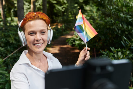A woman in headphones smiles while holding a rainbow flag in the woods.の写真素材