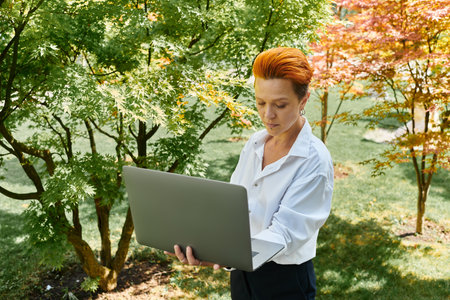 A teacher with short, fiery hair works on her laptop, enjoying the peace of a campus courtyard.