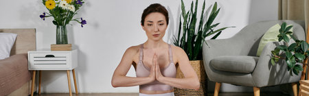 A young woman in a crop top meditates with her eyes closed, sitting in a modern apartment.の写真素材