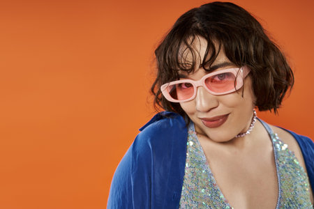 A woman in a vibrant blue outfit and pink sunglasses looks confidently toward the viewer.
