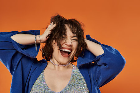 A woman in a blue jacket laughs exuberantly against a vibrant orange backdrop.の写真素材
