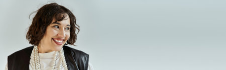 A woman with short, curly hair smiles brightly, wearing a white shirt and a black vest.の写真素材