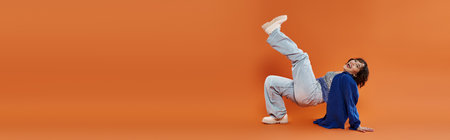 A woman in vibrant attire performs a dynamic dance move against a bright orange background.の写真素材
