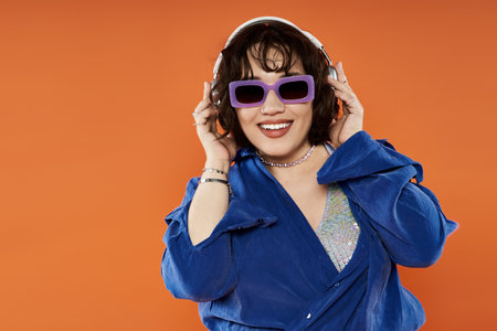 A woman in a blue shirt and purple sunglasses smiles while listening to music with headphones.