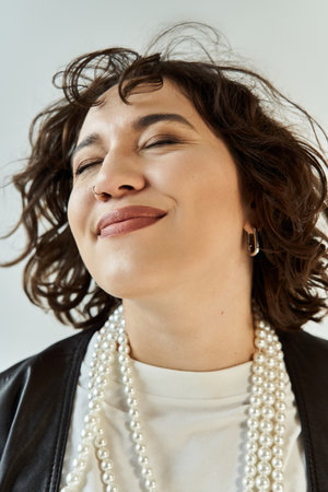 Curly-haired woman in white shirt and black jacket, adorned with pearlsの写真素材