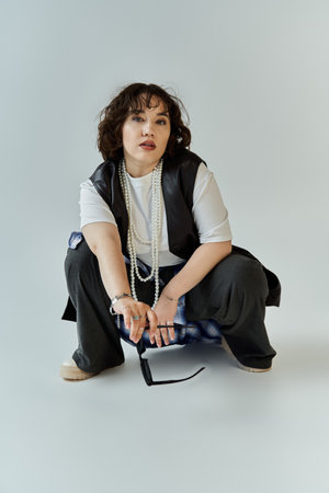 A woman in black pants and a white shirt sits with a thoughtful expression.の写真素材
