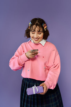 A woman smiles brightly while looking at her phone, holding a gift in her other hand.の写真素材