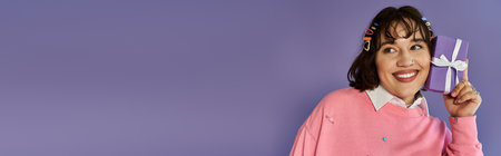 A joyful woman holds a purple gift box to her ear with a big smile.