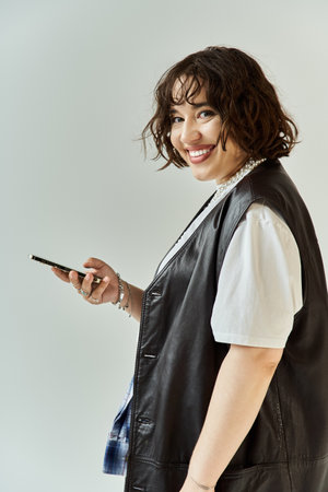 A woman in a leather vest looks at her phone and smiles.