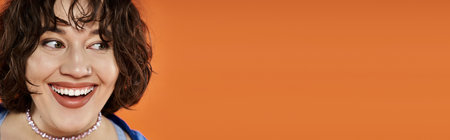 A woman in vibrant attire beams with joy against a bright orange backdrop.の写真素材