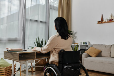 A woman sits in a wheelchair at a desk, looking out a window.