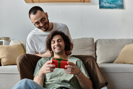 Gay couple cuddles on couch, man opens gift excitedlyの写真素材