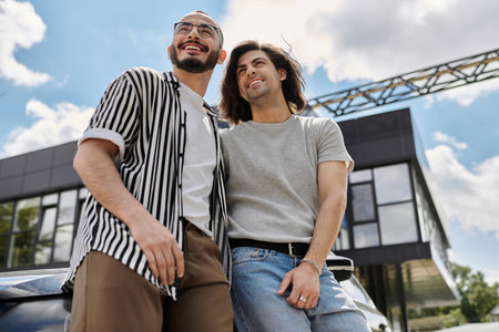 Two men stand close together in an urban setting, looking up and smiling.の写真素材