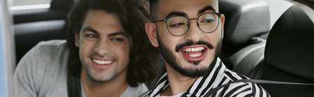 Two men sit in the back seat of a car, smiling and laughing together.
