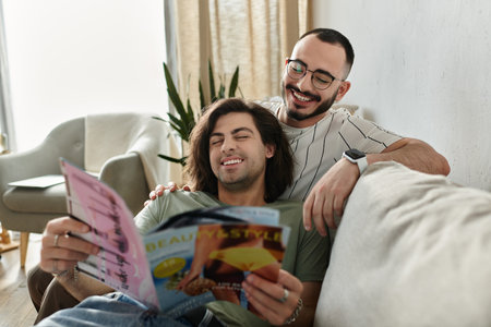 A gay couple relaxes on a couch, laughing together while reading a magazine.の写真素材
