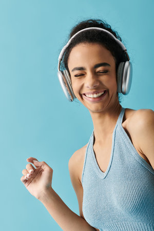 A young woman wearing a blue halter top dances and smiles while listening to music with headphones...