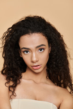 A young woman with dark curly hair and bare shoulders looks directly at the camera.
