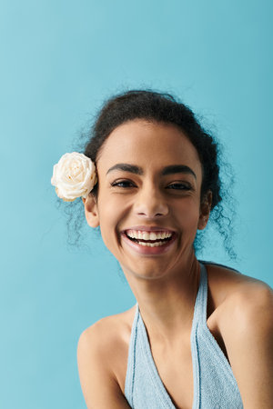 A young African American woman with curly hair and a white flower behind her ear smiles brightly...