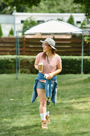 A young woman with a prosthetic leg walks through a park, enjoying a sunny day with a cup of coffee...