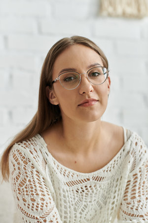 A young woman sits in a white, lace-trimmed sweater, looking at the camera with a thoughtful expression.の写真素材