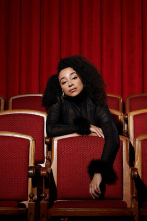 A stylish woman in a black outfit sits in a red velvet cinema seat, engrossed in a film.