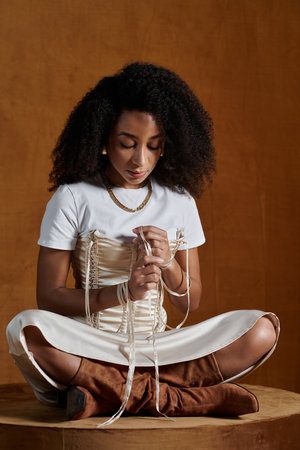 A stylish African American woman sits in a studio, her fingers gently adjusting the straps of her...