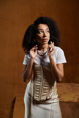 An African American woman wearing a white shirt and a satin corset poses in a studio setting, her gaze directed upwards.の写真素材