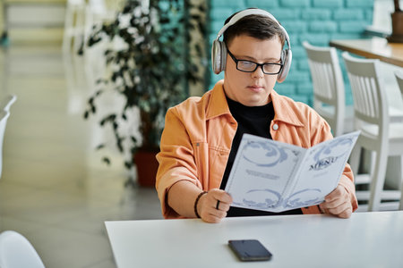 A man with Down Syndrome sits at a table in a cafe, thoughtfully reviewing the menu.