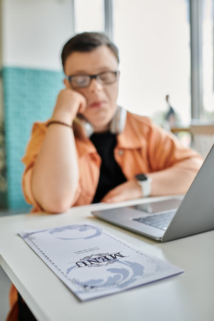 A man with Down syndrome works on his laptop in a cafe, showcasing the increasing diversity of the freelance workforce.の写真素材