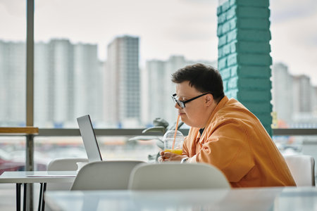 A man works remotely on his laptop in a cafe, enjoying a drink while taking in the city view.の写真素材