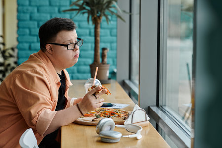 A man with Down syndrome savors a slice of pizza while enjoying a cafe.の写真素材